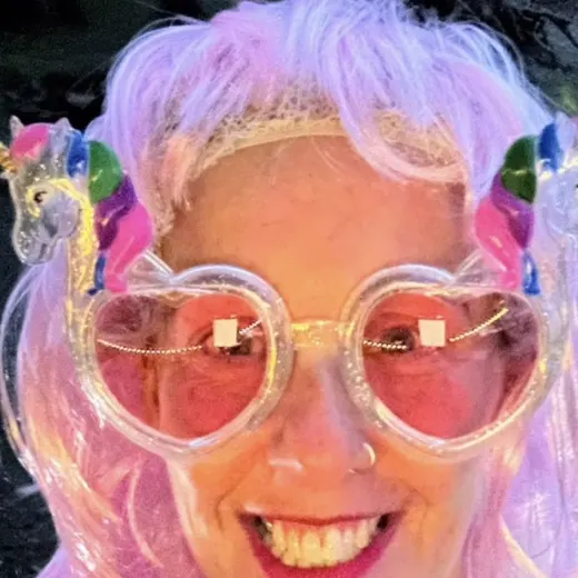 A swimmer in a pink wig and heart sunglasses grinning at the camera