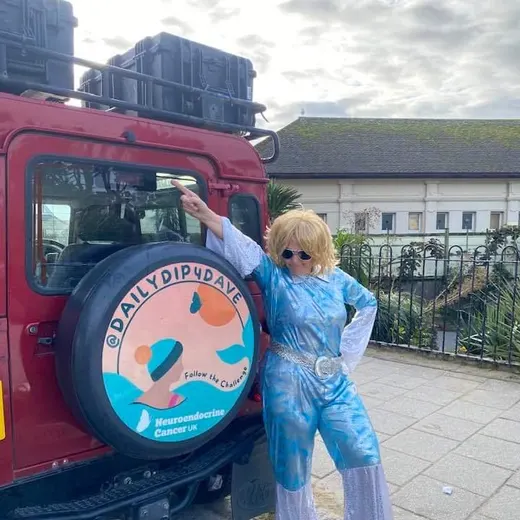 A swimmer in sparkly blue next to a decorated Land Rover