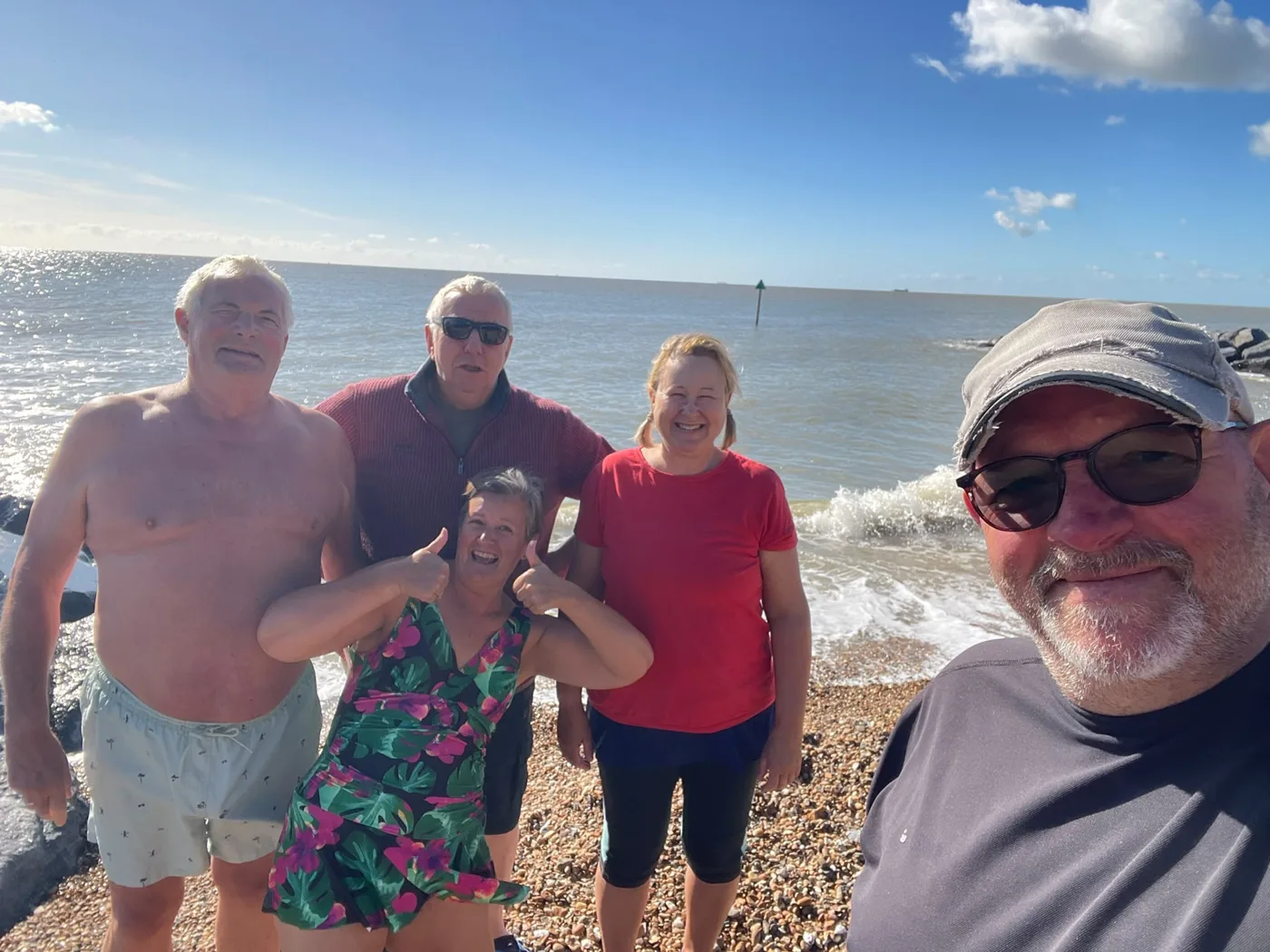 A group of friends giving thumbs up on a pebble beach after their dip