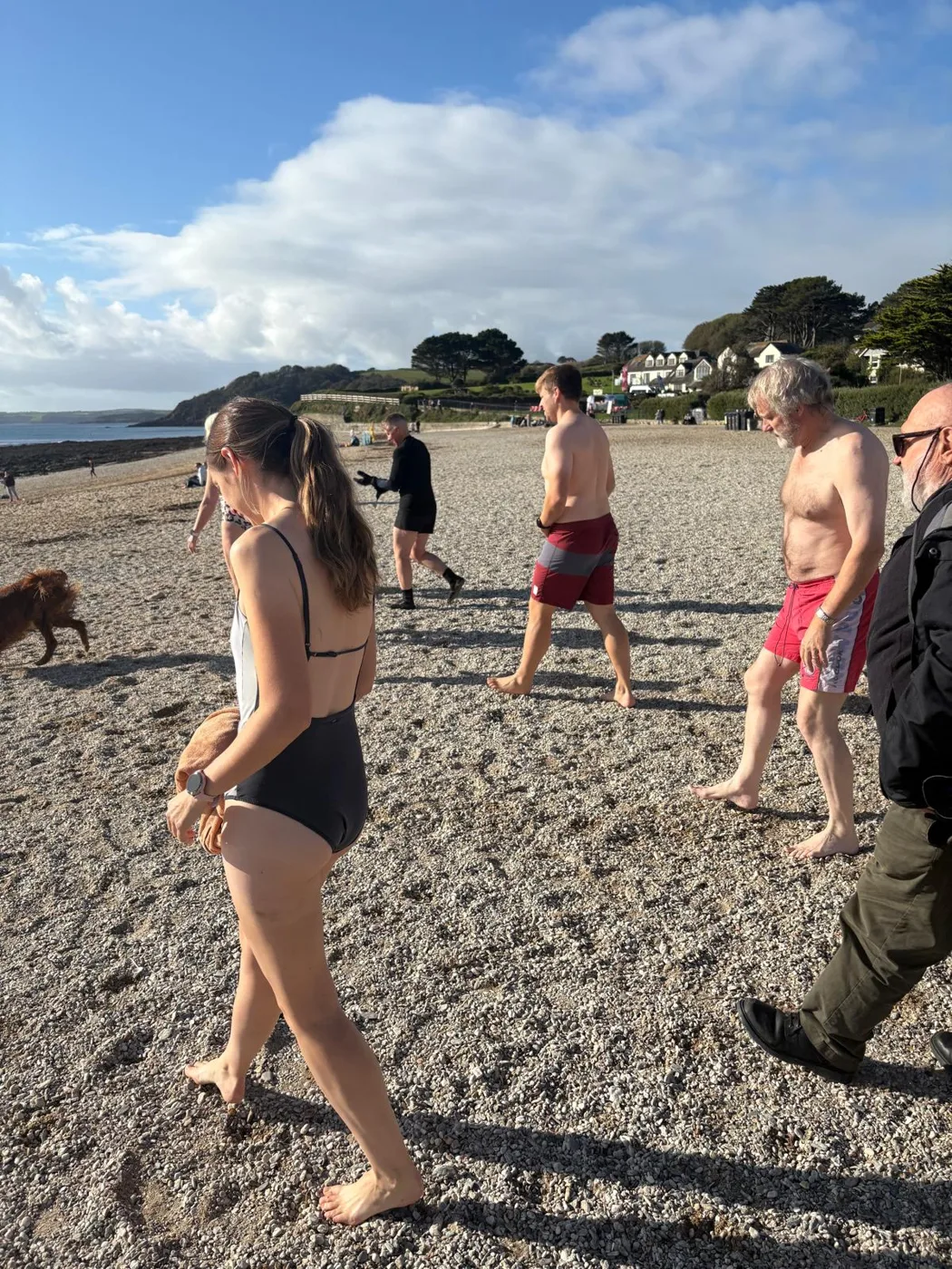 Swimmers walking down the shingle towards the water