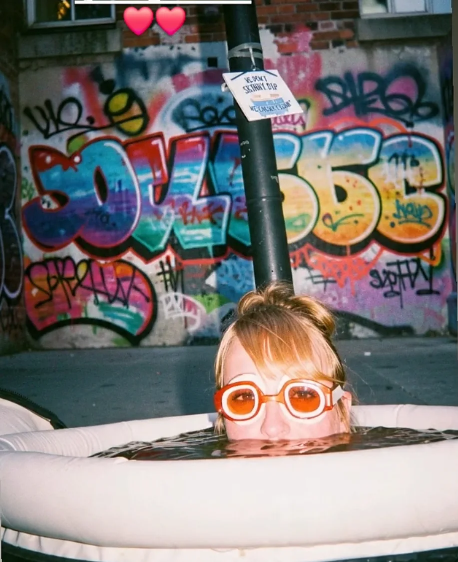 A swimmer in orange goggles in an inflatable tub in front of graffiti